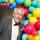 A performer wearing a tuxedo stands in front of a display of multi-coloured balloons.
